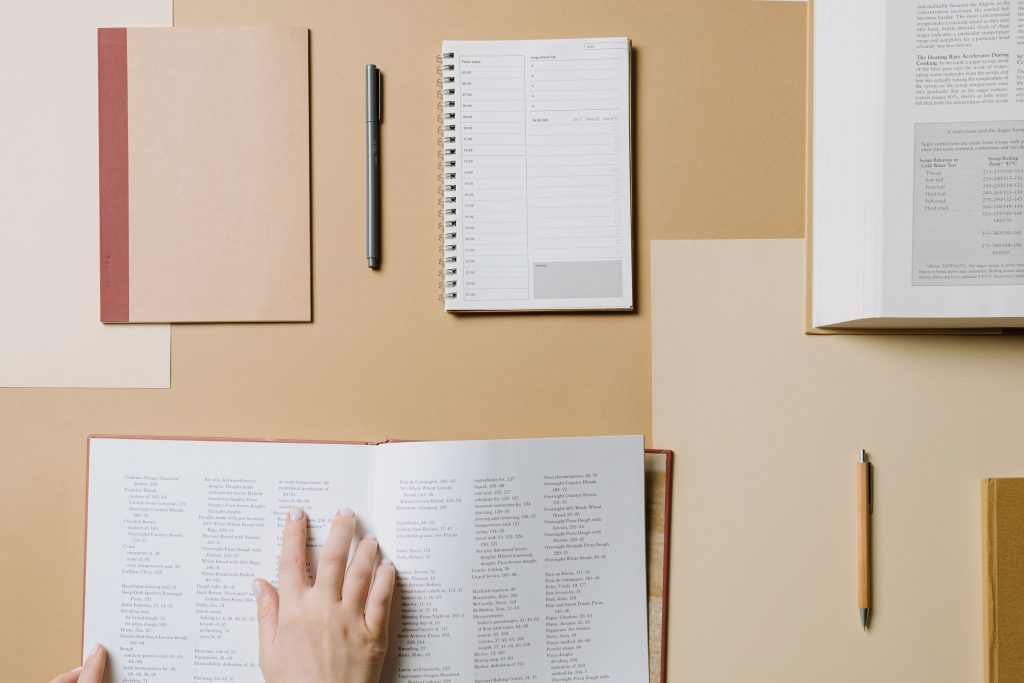 A top view of books and stationery on a beige desk for workflow inspiration.