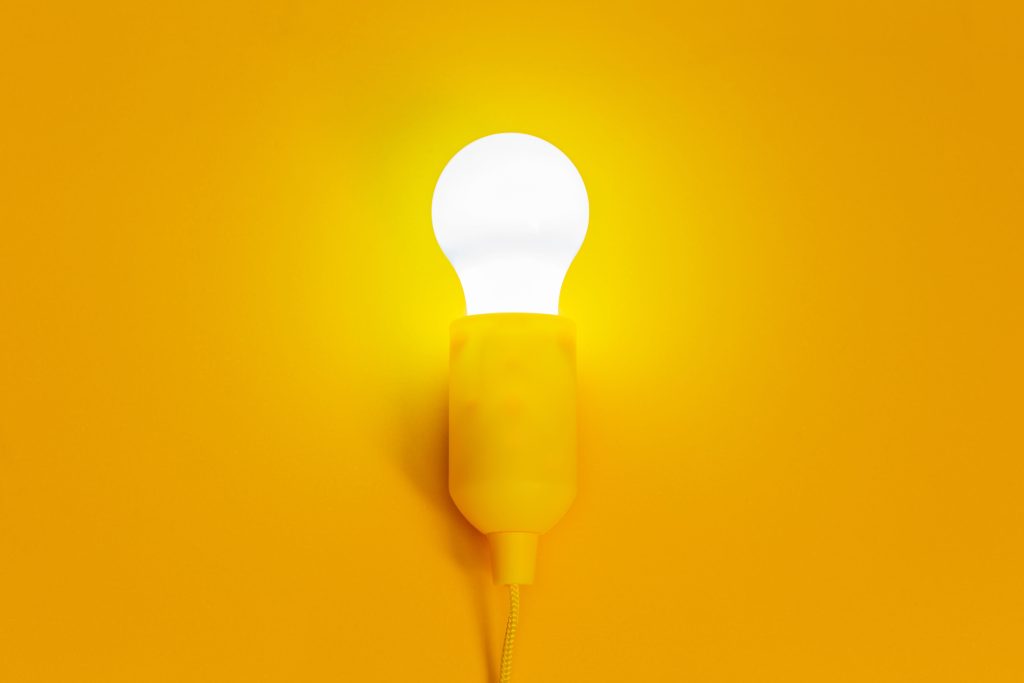 Illuminated light bulb with a vibrant yellow background, symbolizing ideas and inspiration.